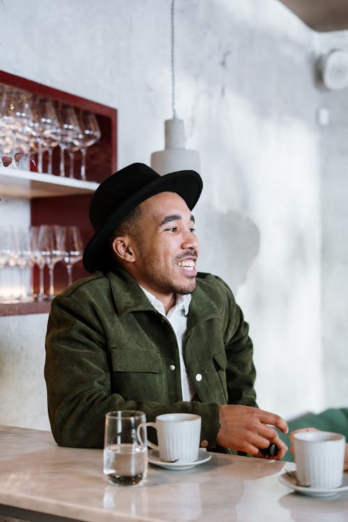 Man in Green Button Up Shirt Wearing Black Hat Sitting on Chair
