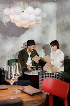 一对夫妇坐在时尚咖啡馆的桌旁，在独特的吸顶灯下看着菜单点单