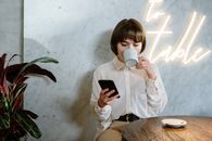 在霓虹灯的氛围下，一位年轻女子在时尚的咖啡馆里，边喝咖啡边用着手机