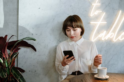 Woman in White Long Sleeve Shirt Holding Black Smartphone