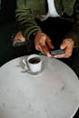 男子在大理石桌面的咖啡桌旁，用智能手机对着一杯咖啡