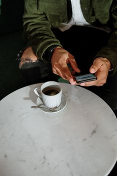 男子在大理石桌面的咖啡桌旁，用智能手机对着一杯咖啡