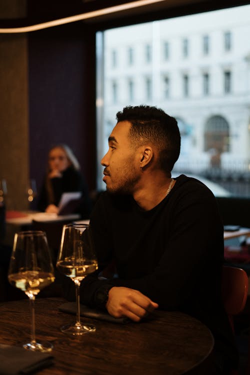 Man in Black Long Sleeve Shirt Sitting Beside Table With Wine Glass