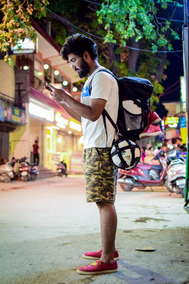 Sportive Guy With Backpack Using Phone On Night Street