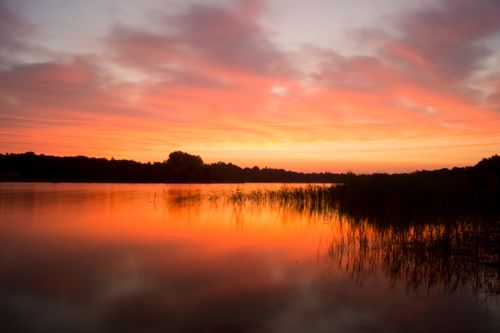 Free Beautiful sunset reflecting over a calm lake with vibrant colors and gentle clouds. Stock Photo