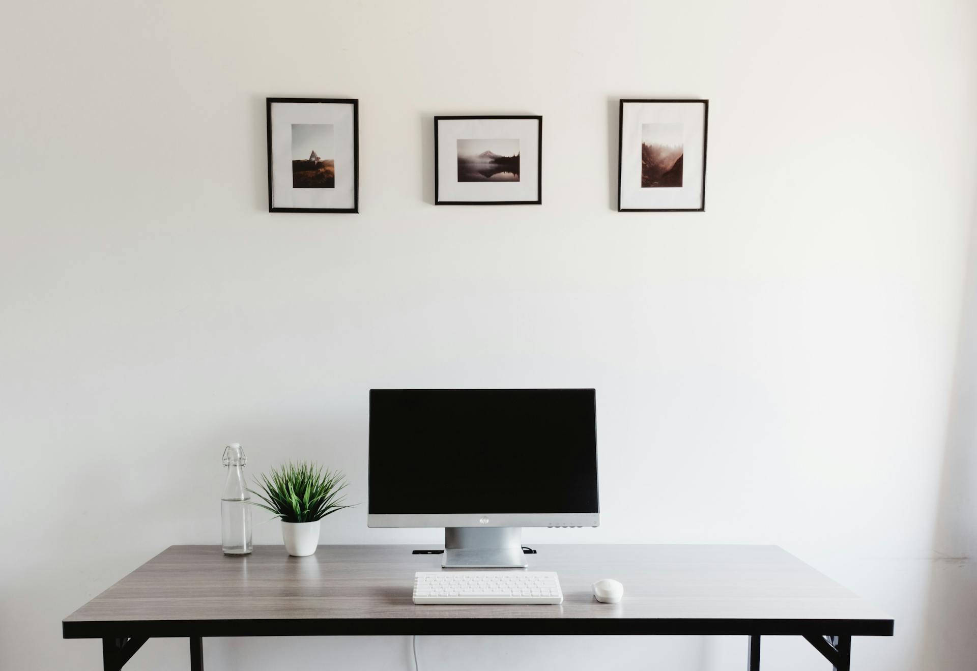 A sleek minimalist desk setup with computer, keyboard, mouse, and wall art.