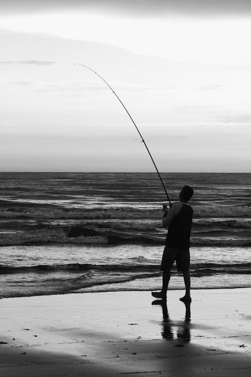 

A Grayscale of a Man Shore Fishing