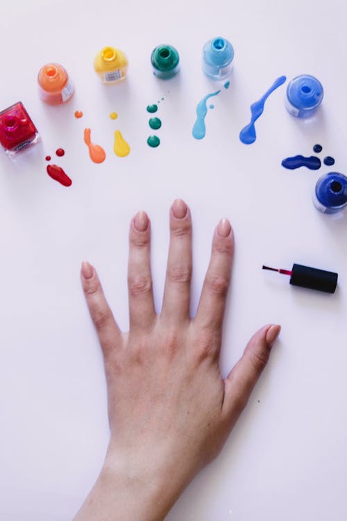 From above of crop unrecognizable female demonstrating hand with manicure and choosing bright color from set of rainbow spectrum nail varnishes