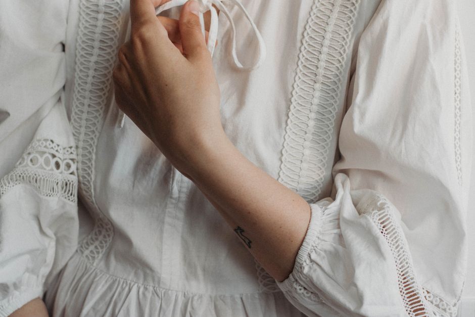 Crop anonymous female in white traditional decorated handmade linen wear with crumpled sleeves and thin cords at home