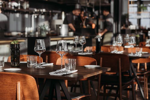 From above of classic style cafe interior with wooden chairs and shiny glasses near cutlery on cloth napkins on table in daylight