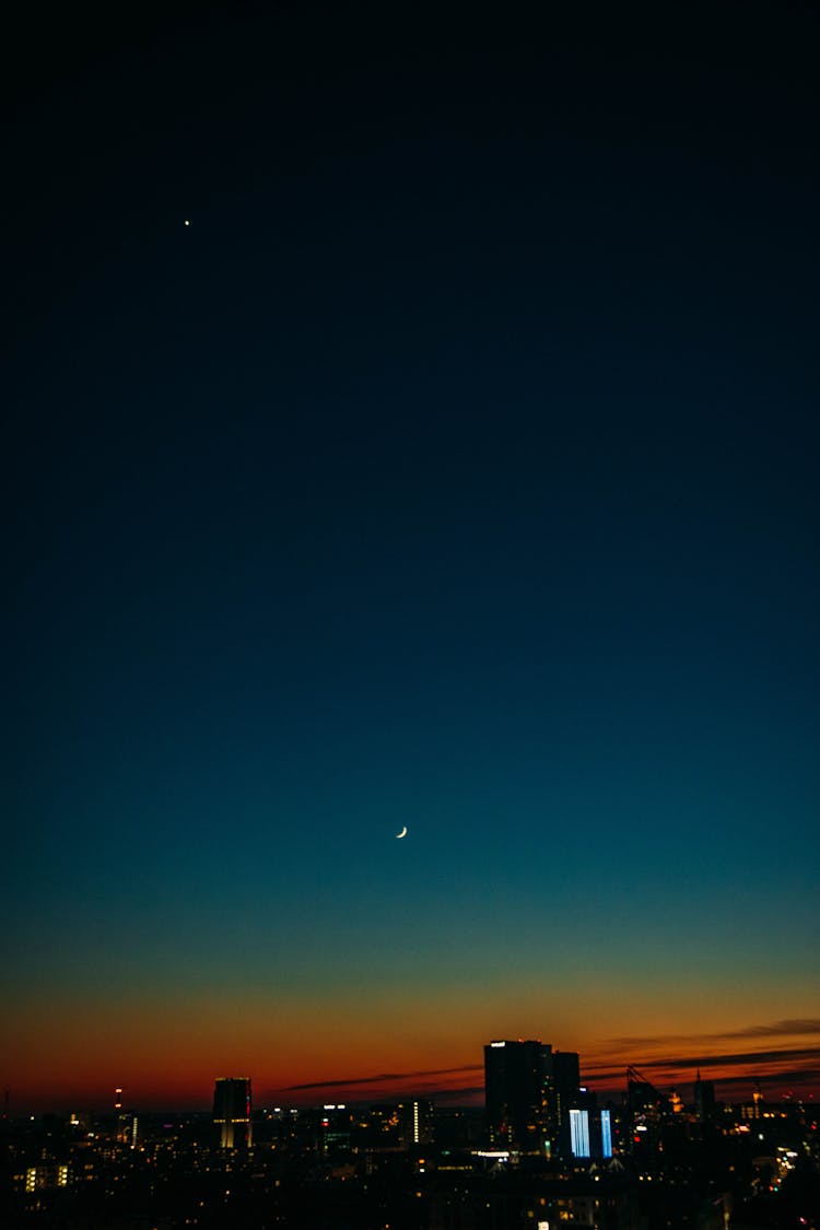 Colorful Night Sky With Moon Above City Buildings At Sunset