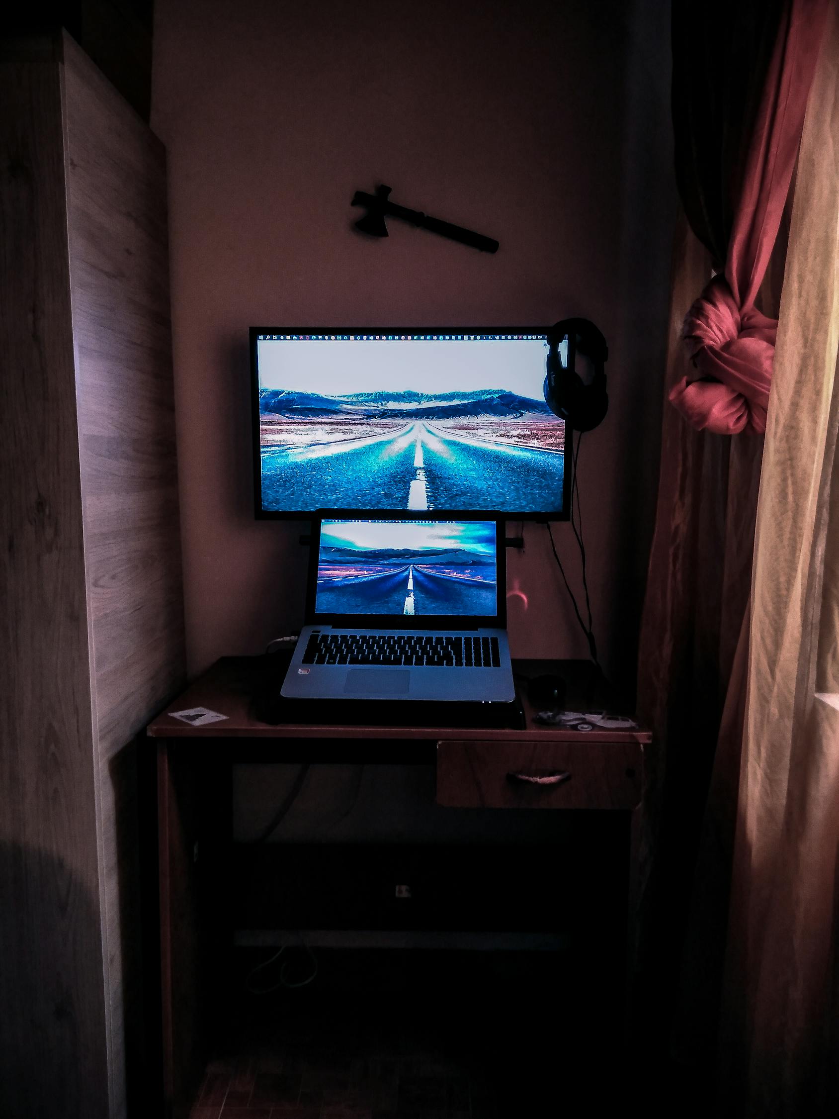 Modern design computer and netbook with photo of straight asphalt road behind mountains on screens in dark room in apartment