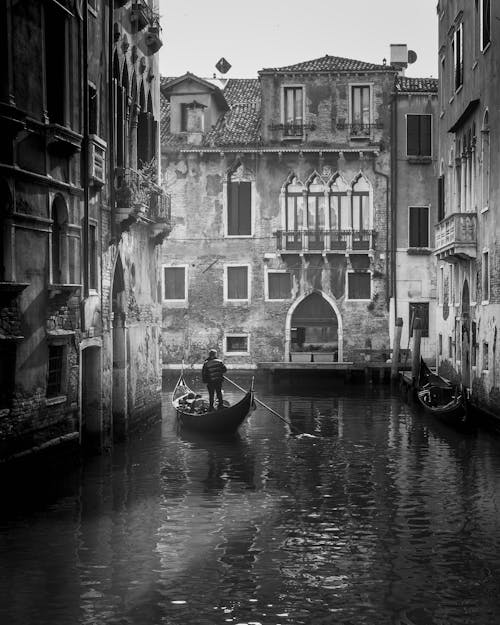 
A Grayscale of a Person Riding a Gondola on a Canal