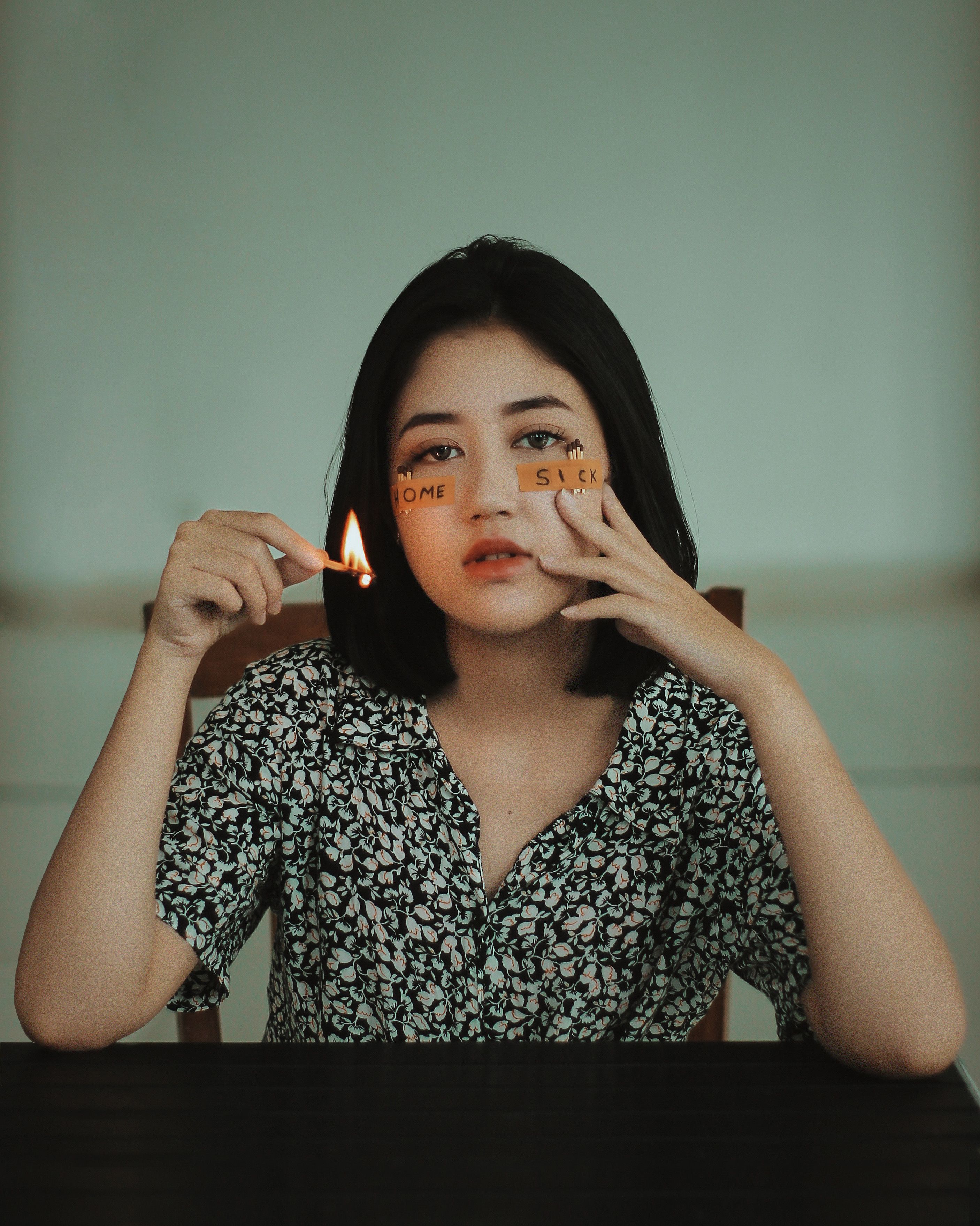 一位年轻女子在室内手持点燃的火柴，轻抚脸颊，流露出忧郁与思乡之情