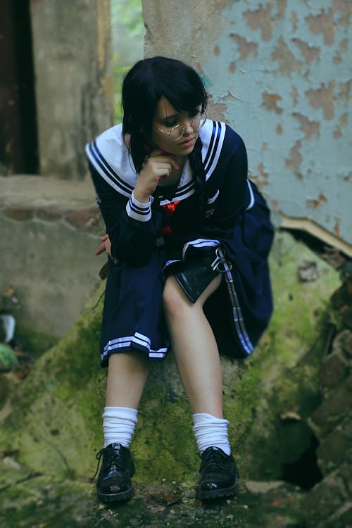 Pondering ethnic teenager in school uniform sitting on mossy stone