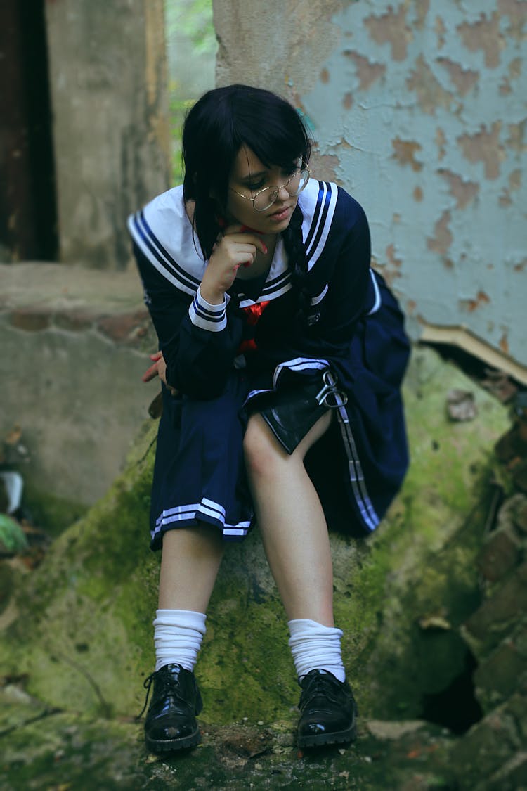 Pondering Ethnic Teenager In School Uniform Sitting On Mossy Stone