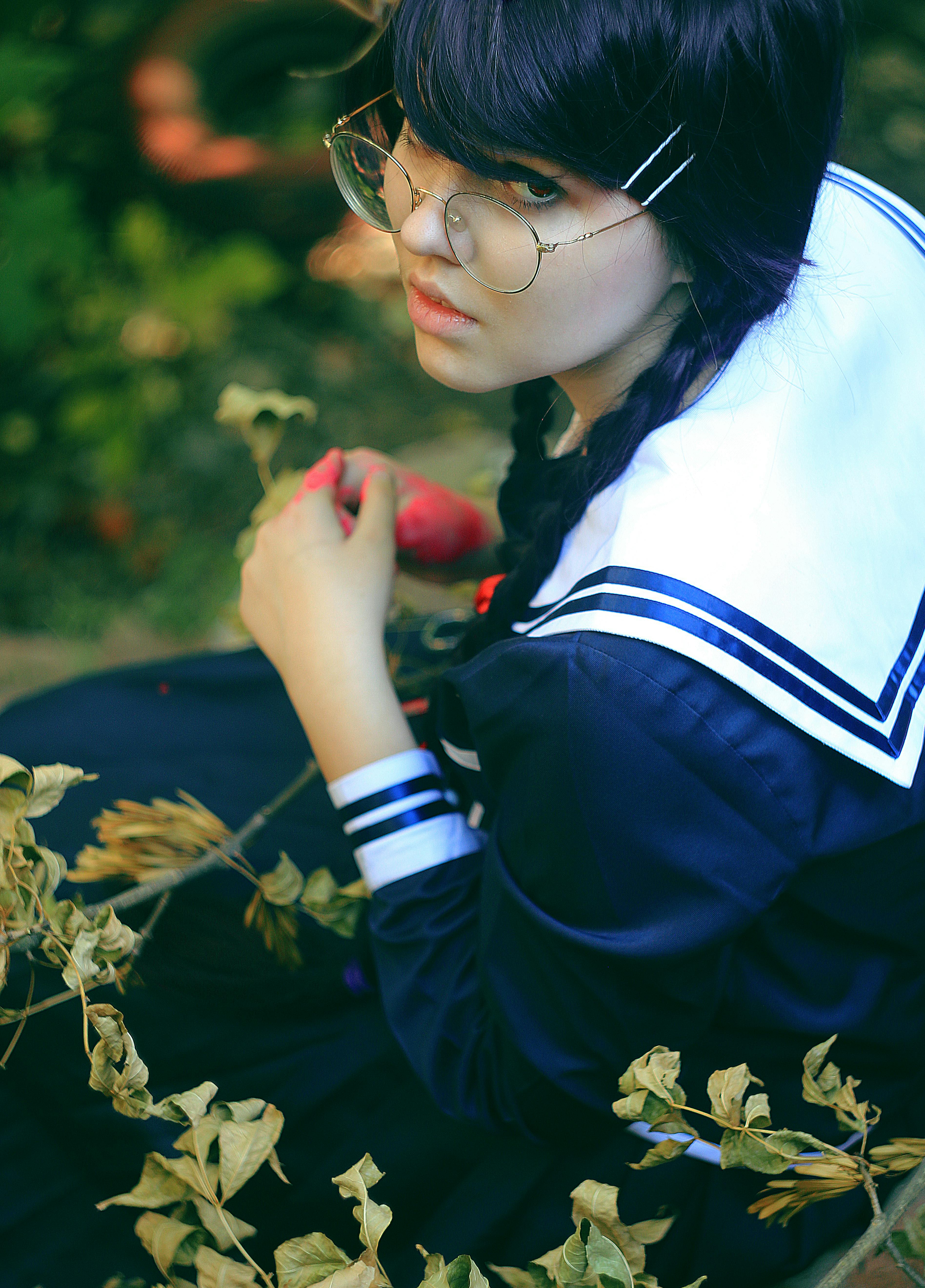 一位戴着眼镜、穿着水手校服的年轻女子，坐在户外的树叶间