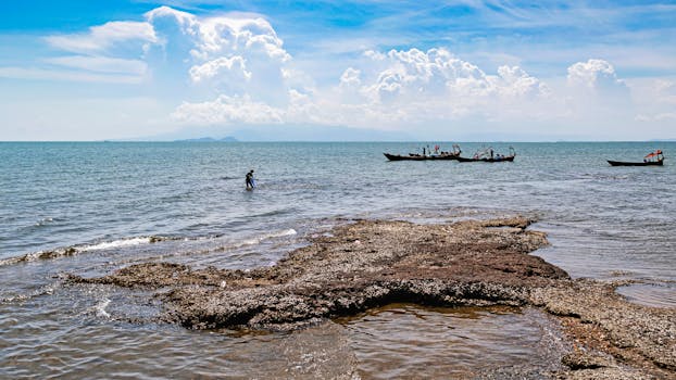 Scenic view of boats near rocky shore under a cloudy sky in Kep, Cambodia.