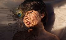 一个女人闭着眼睛，在孔雀羽毛的阴影下享受阳光