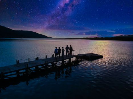 站在星空下，平静的涟漪湖水附近的码头上，匿名者的后视图
