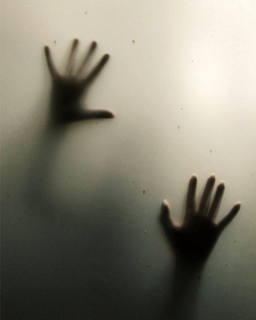 Mysterious silhouette of hands pressing against a frosted glass surface, evoking intrigue.