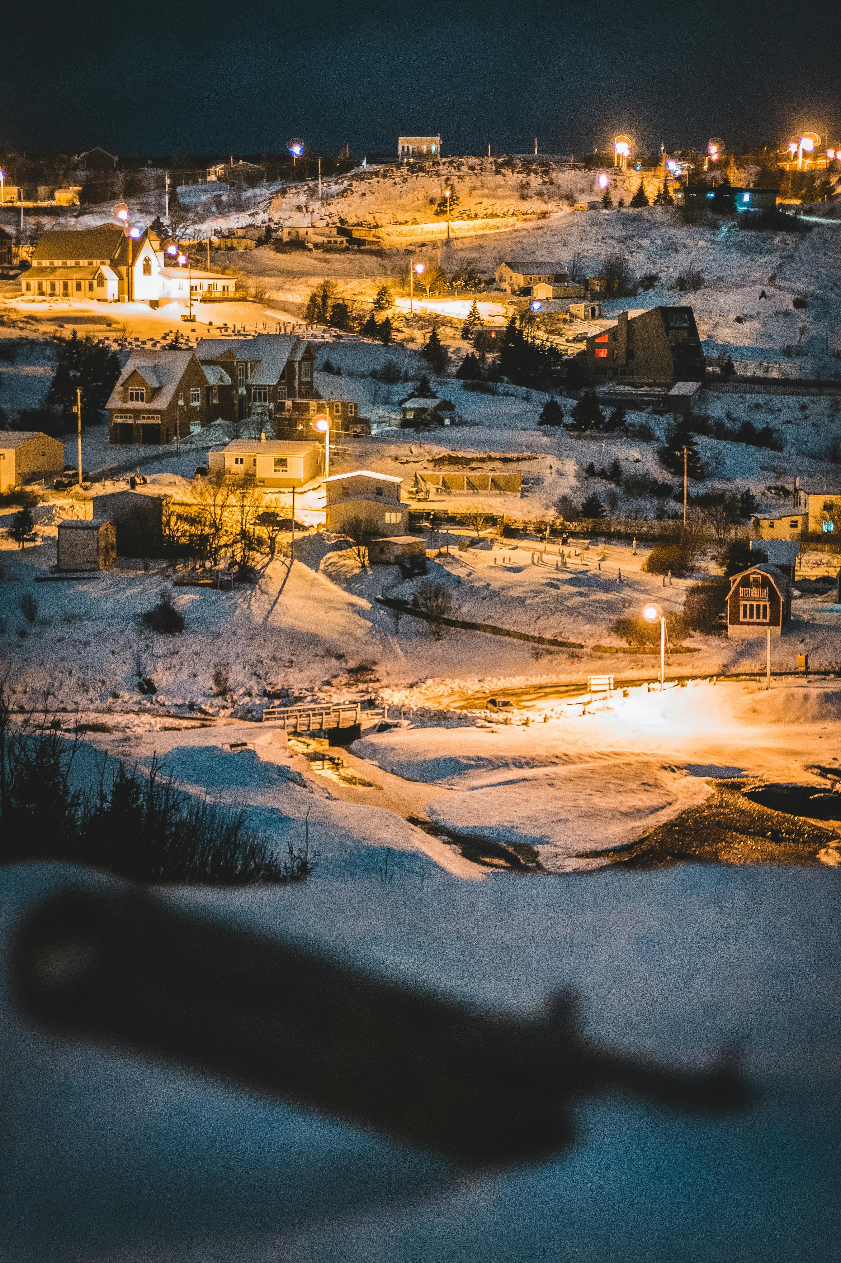 Illuminated houses in snowy valley among lights under dark sky of winter night
