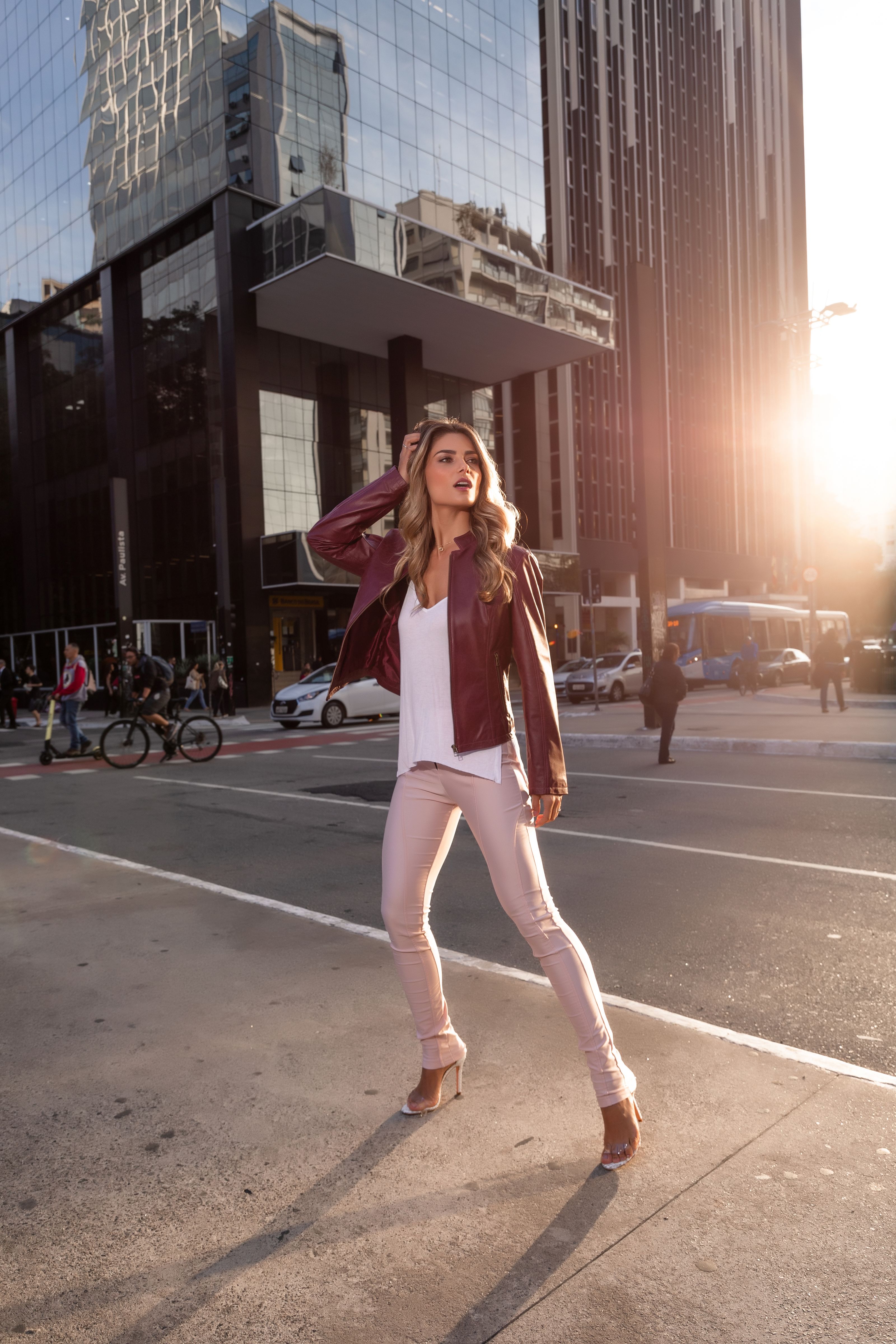 Mulher estilosa com roupa da moda posando na rua da cidade com um cenário de pôr do sol.