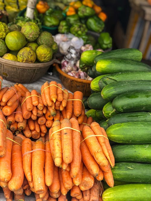 High angle various fresh organic vegetables including carrots cucumbers and garlic arranged on table for sale in outdoors market