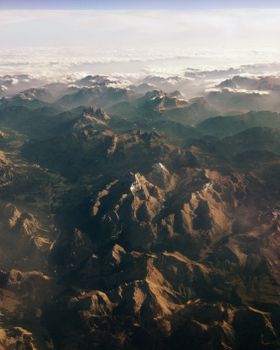 Breathtaking aerial shot of mountain ranges at dawn with clouds and sunlight casting shadows.