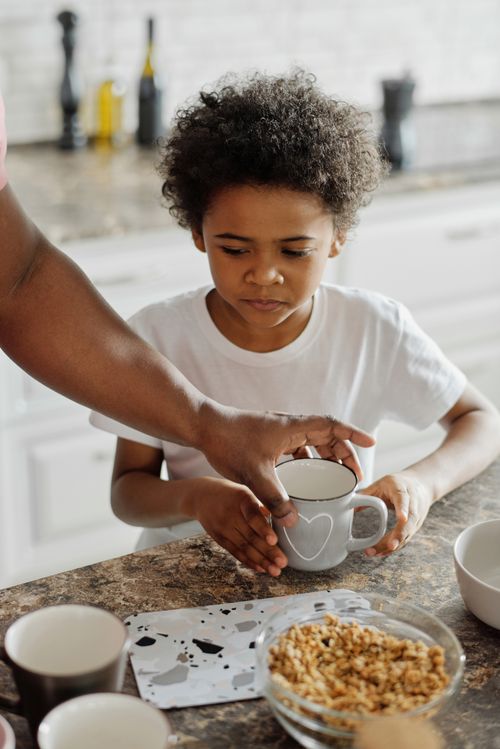 Free A child holds a cup on a kitchen counter during breakfast time, sharing a moment with family. Stock Photo