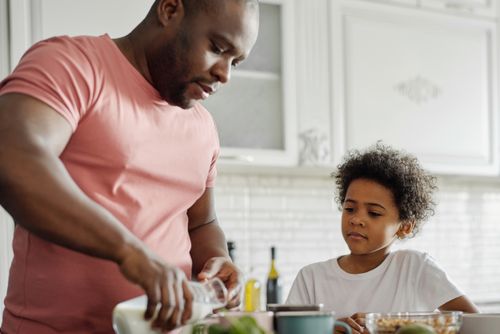 Free Father pouring milk with son watching in a cozy kitchen setting. Stock Photo