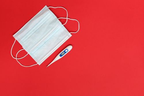 Free Flat lay of a surgical mask and digital thermometer on a red background, symbolizing health and safety. Stock Photo