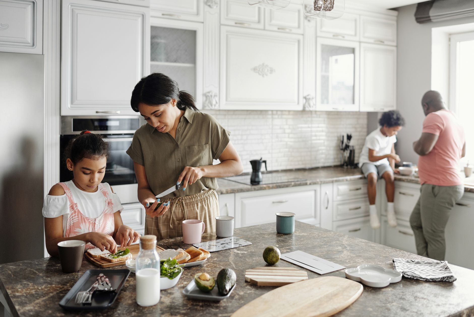 地中海飲食實踐:孩子飲食教育的有效策略 A mother and daughter preparing avocado toast in a bright kitchen while the father and son interact in the background.