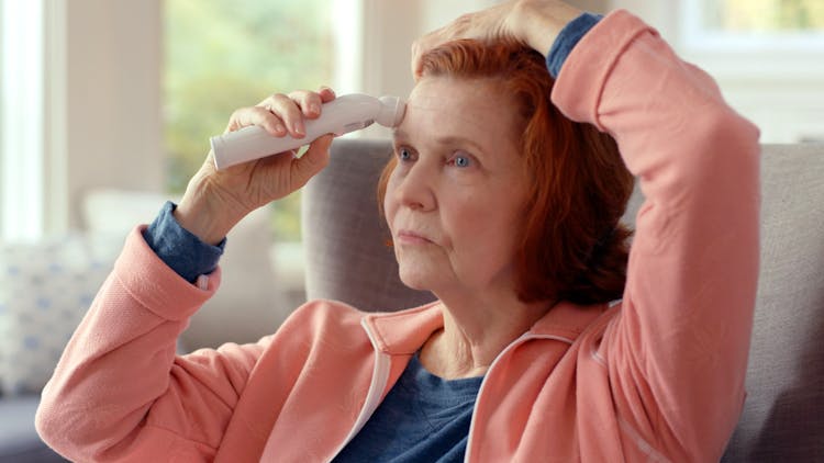 Close-Up Shot Of An Elderly Woman In Peach Jacket Holding A Thermometer