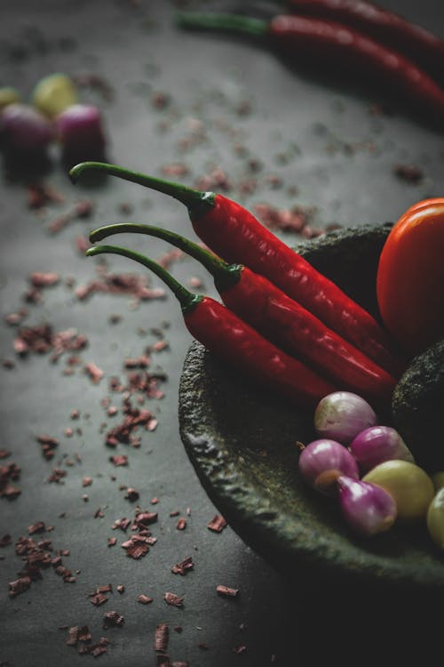 Free From above of red hot chili peppers placed in stone bowl with fresh onions and vegetable served on table with scattered spices Stock Photo