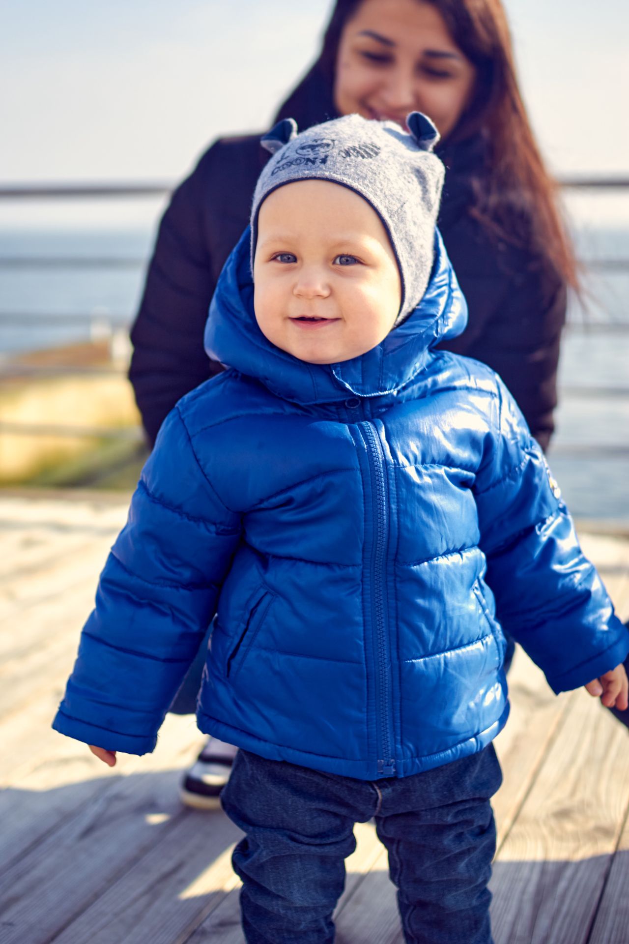 Toddler in a shiny blue puffer jacket and gray animal-ear hat