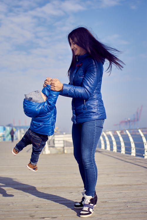 Photo of a Mother in a Blue Jacket Playing with Her Child Outdoors