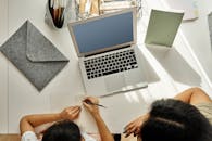 母亲在室内用笔记本电脑帮助女儿在桌子上做作业