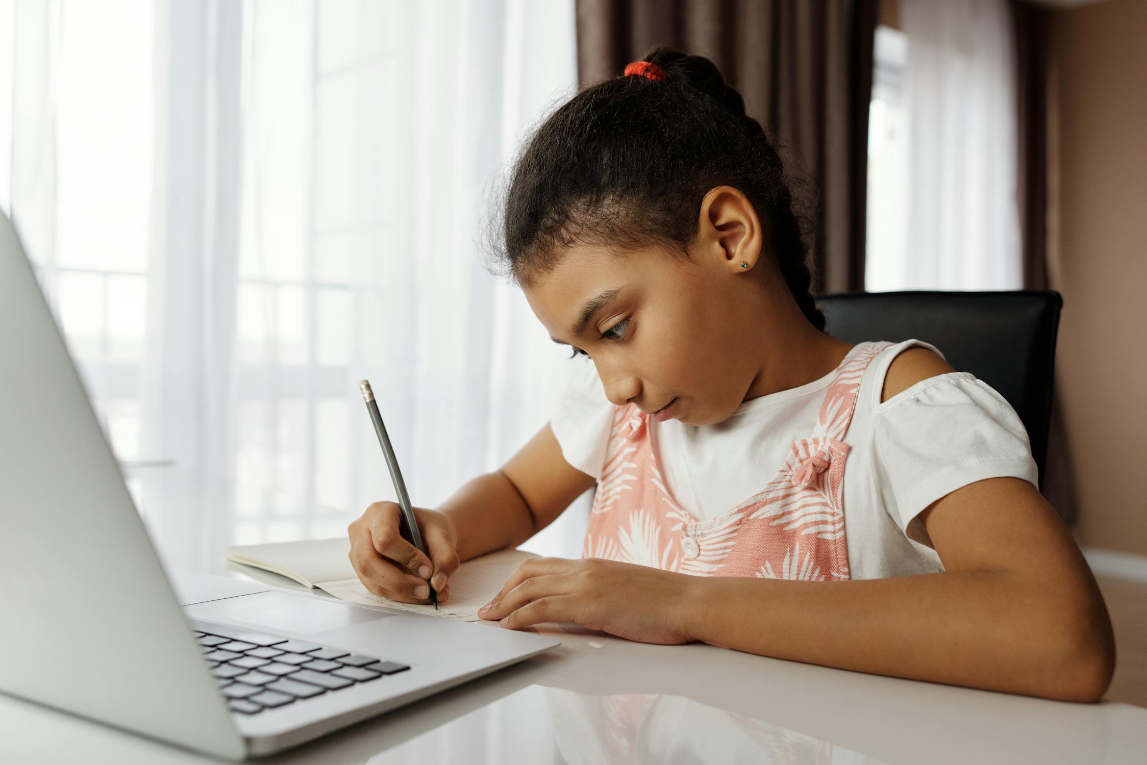 A young girl takes notes while taking part in remote learning