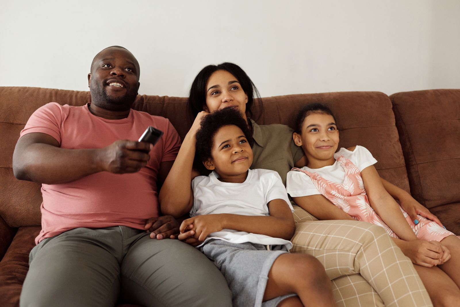 A family smiling together on the couch while watching TV