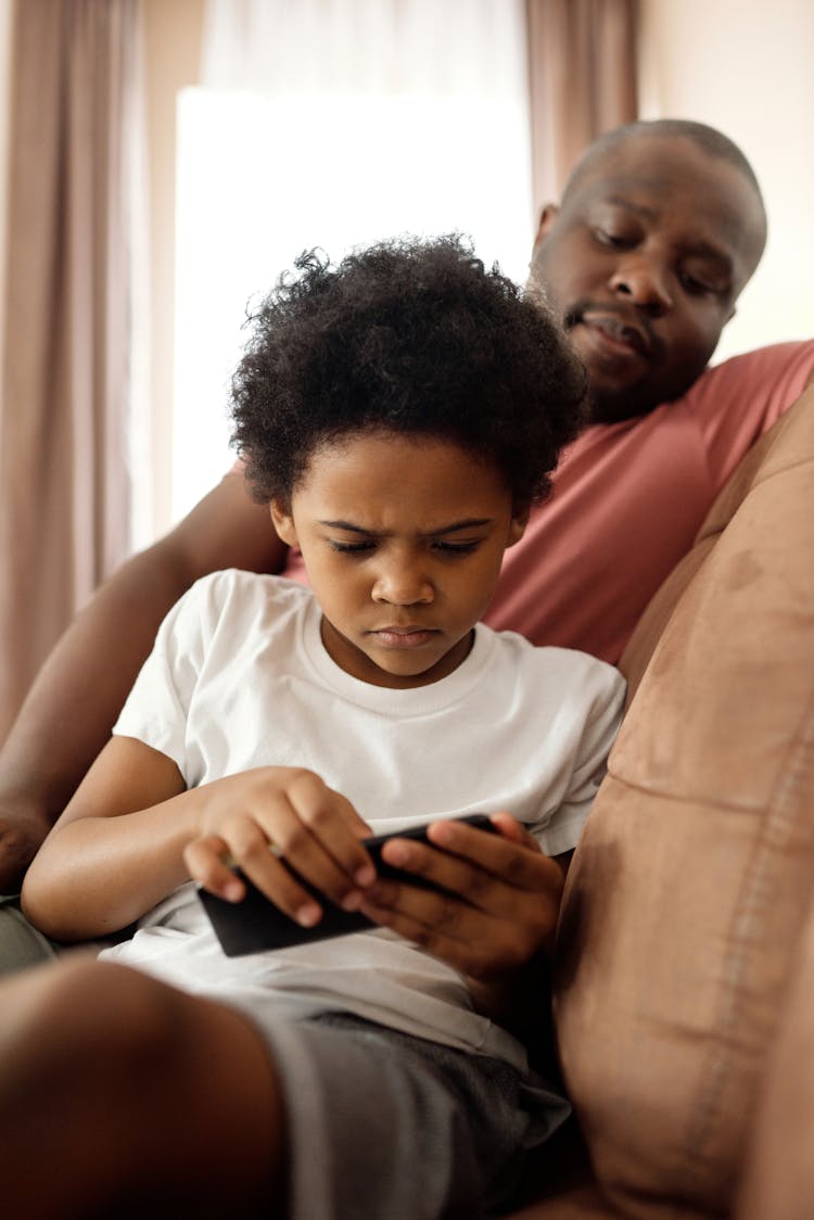 Father Looking At His Son Playing On A Smartphone