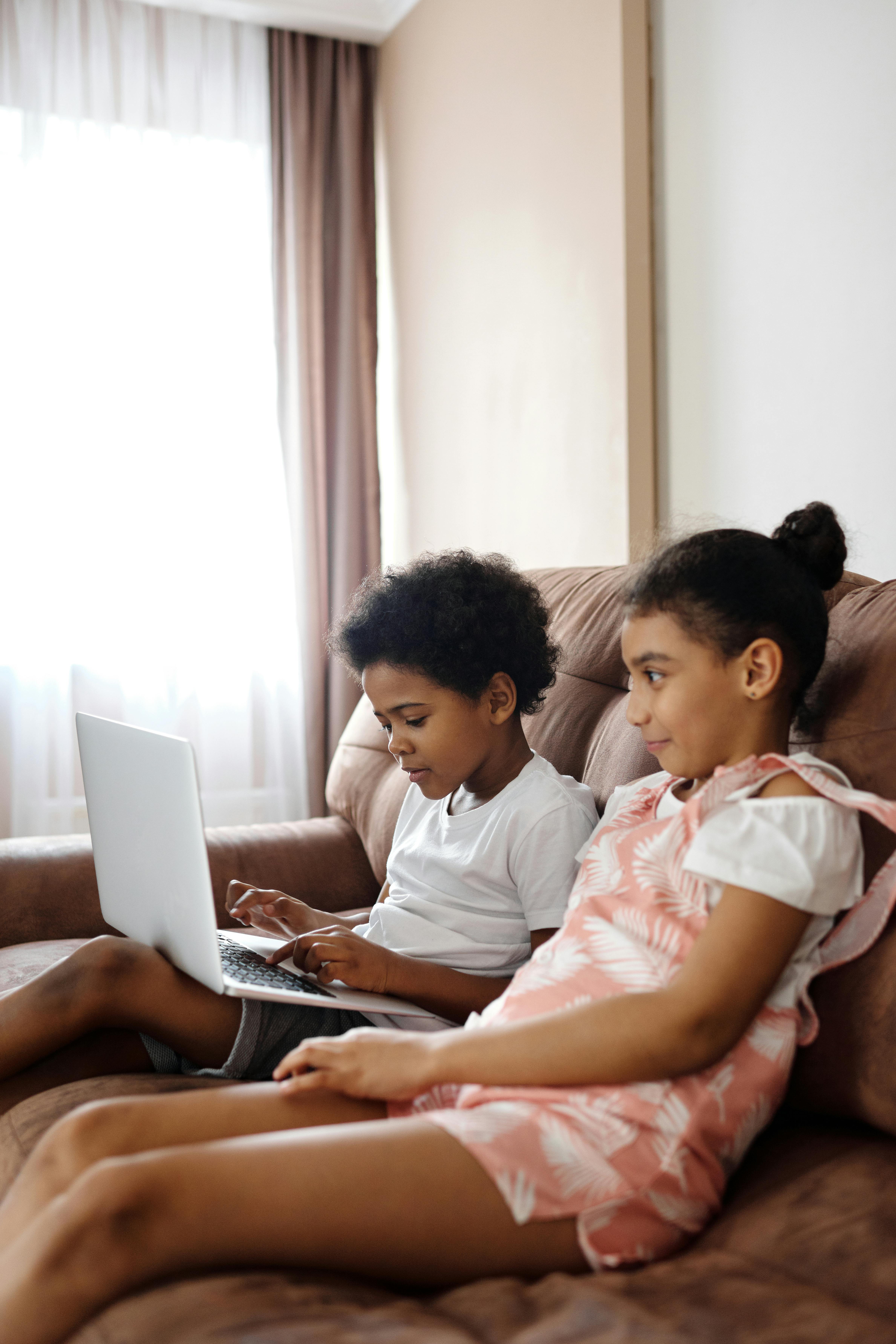 siblings sitting on a couch and looking at a laptop