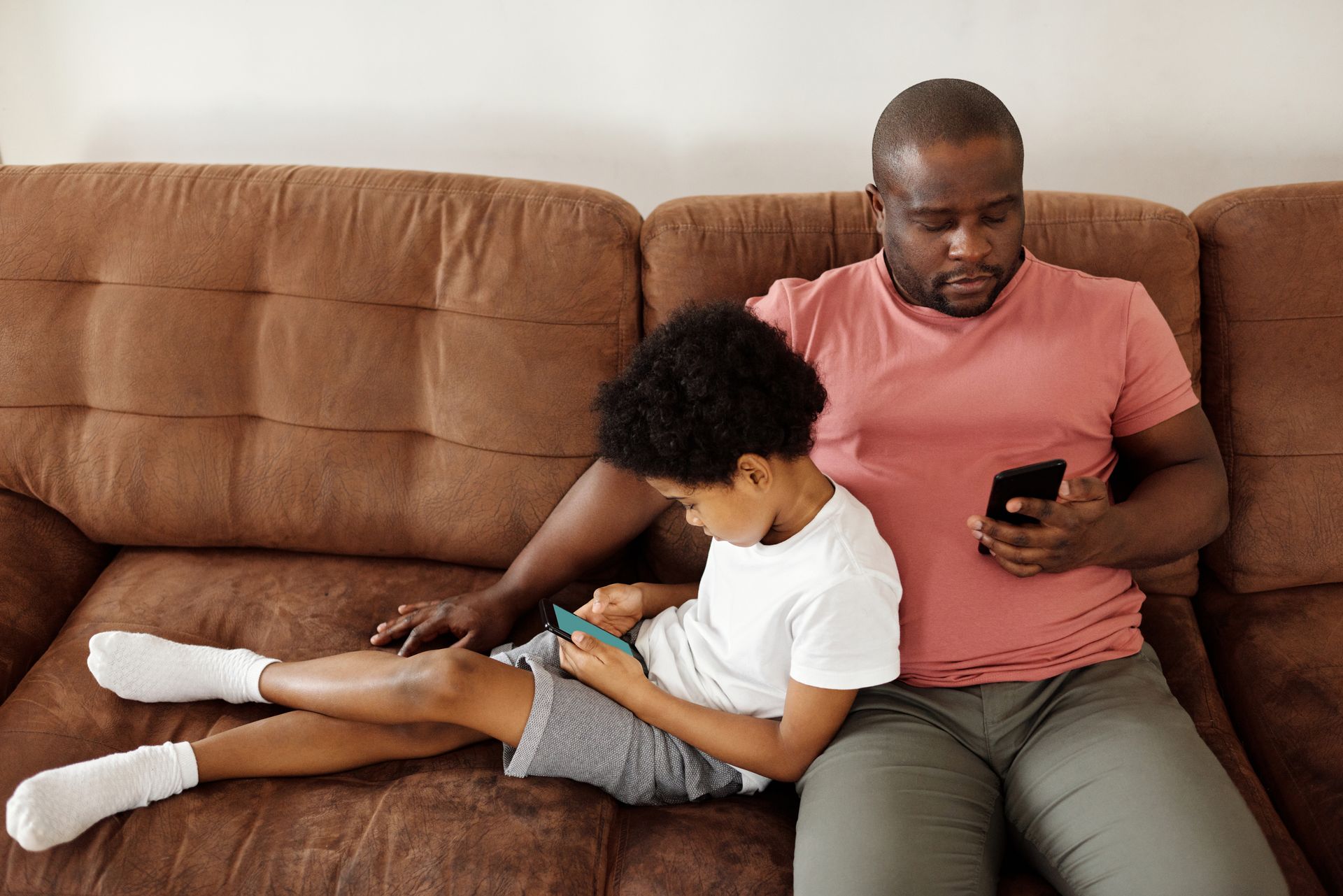 Father and son bonding over smartphones while relaxing on a comfortable couch at home.