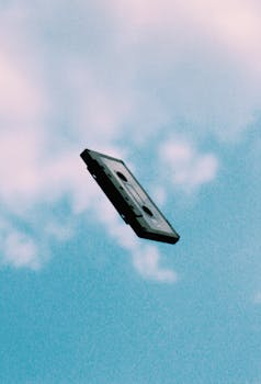 A nostalgic cassette tape captured floating against a backdrop of a blue sky and white clouds.