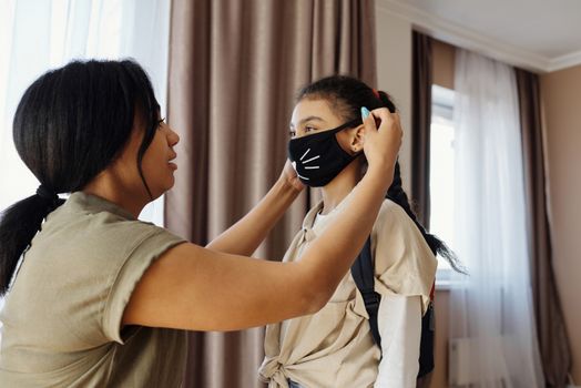 母亲在室内帮女儿戴口罩以确保安全