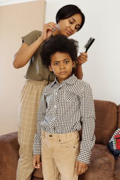 A mother styling her son's curly hair with a hairbrush indoors, capturing a warm family moment.