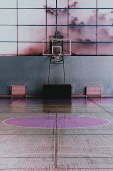 Small basketball hoop under big broad light pink window in bright spacious sports hall