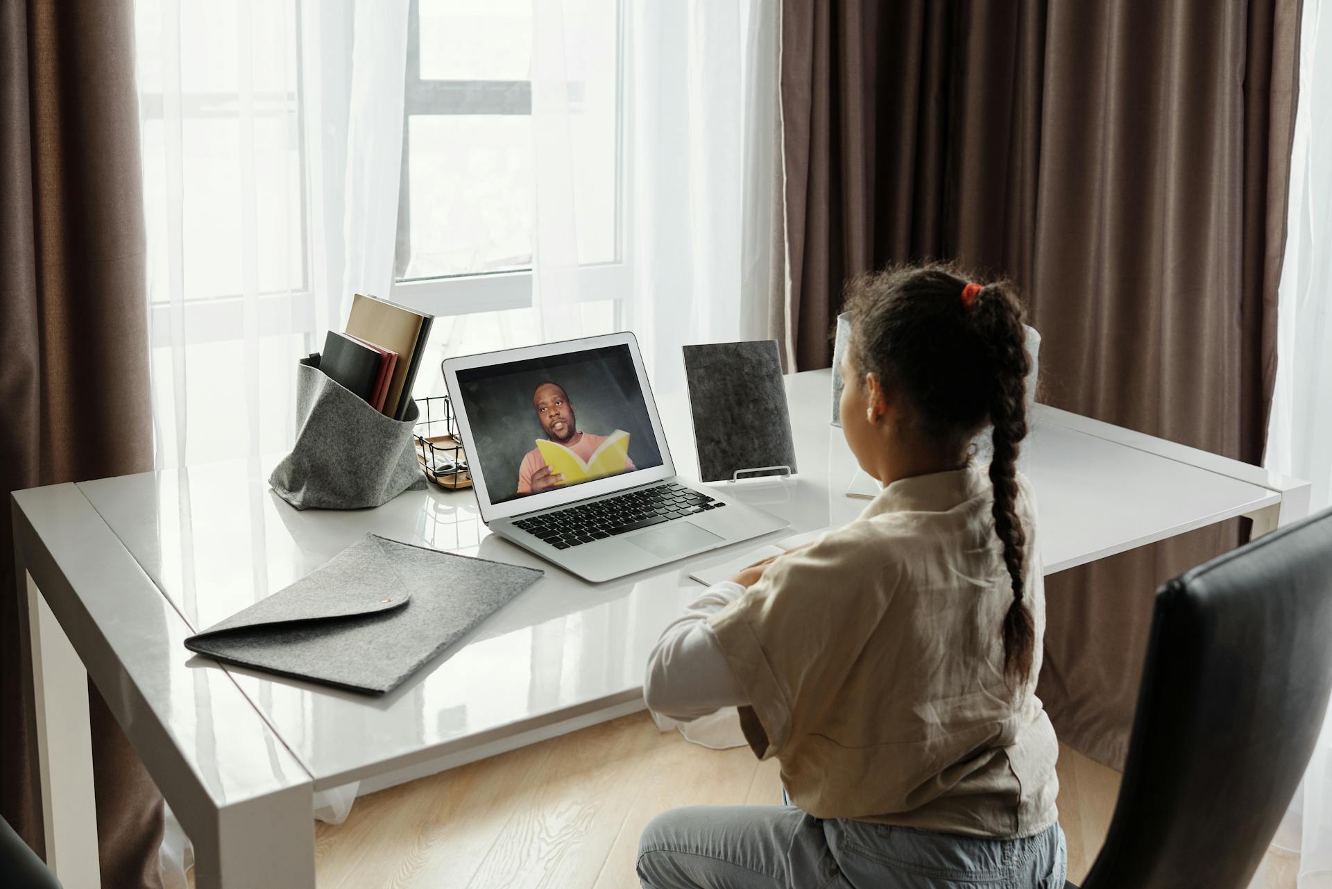 Young girl engaged in a virtual learning session at home with a teacher on video call.