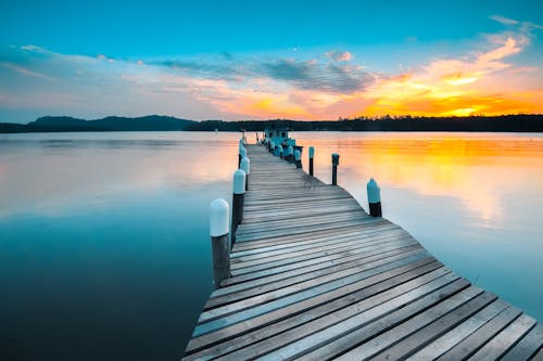 Picturesque view of vivid sundown above forest and long wooden pier above calm reservoir