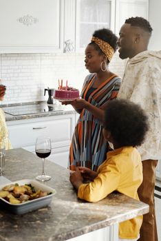 A joyful family gathering around a birthday cake in a modern kitchen setting.